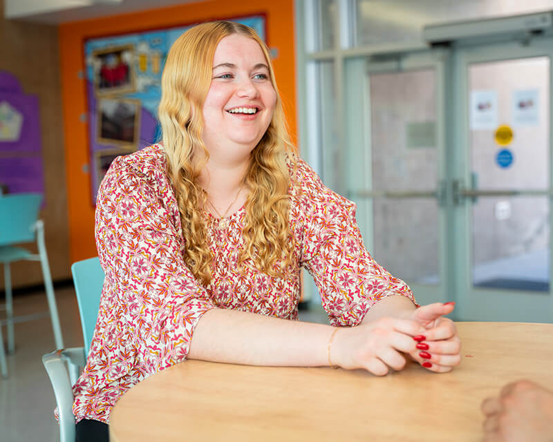 Student at a cafeteria table talking to someone behind the camera.