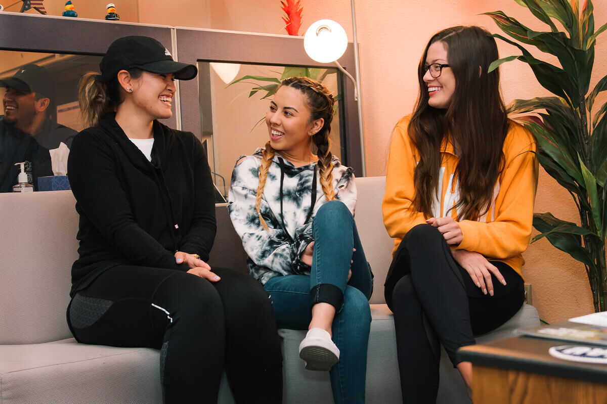 Three woman sit in a lounge smiling and chatting at a campus