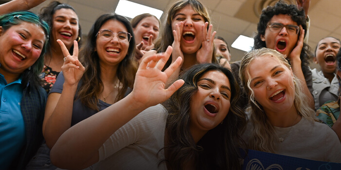 A group of students cheering and holding a Pima Community College banner.