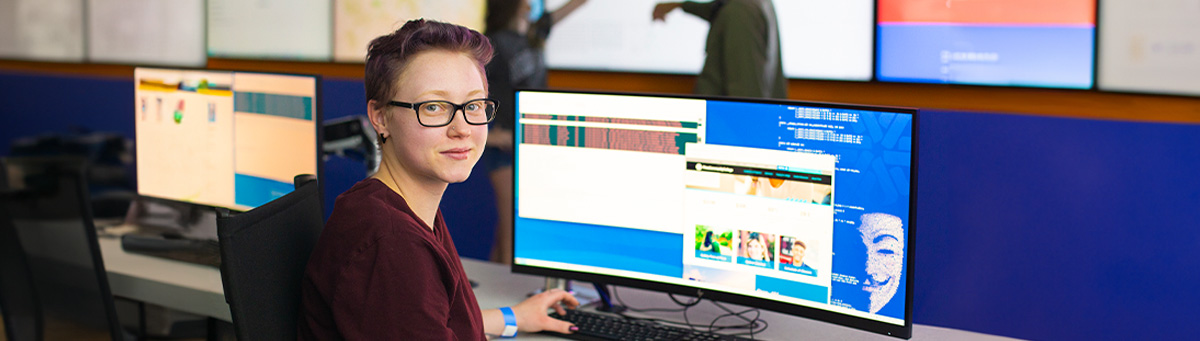 A student sits smiling at computers in Pima's IT Center of Excellence