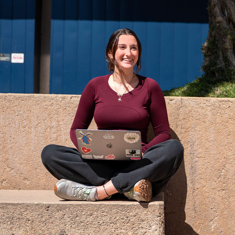 Julia sits on her laptop in a campus breezeway