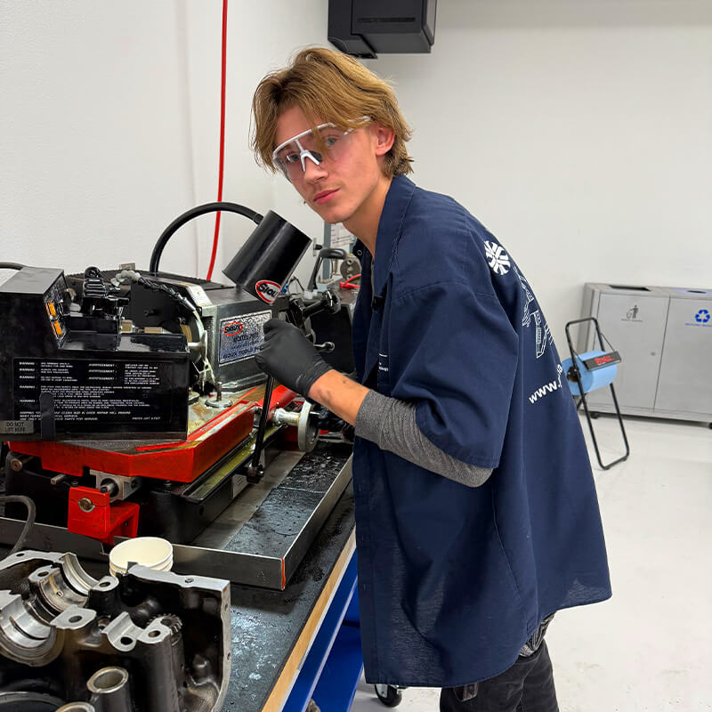 Dylan works on an airplane engine, smiling at the camera